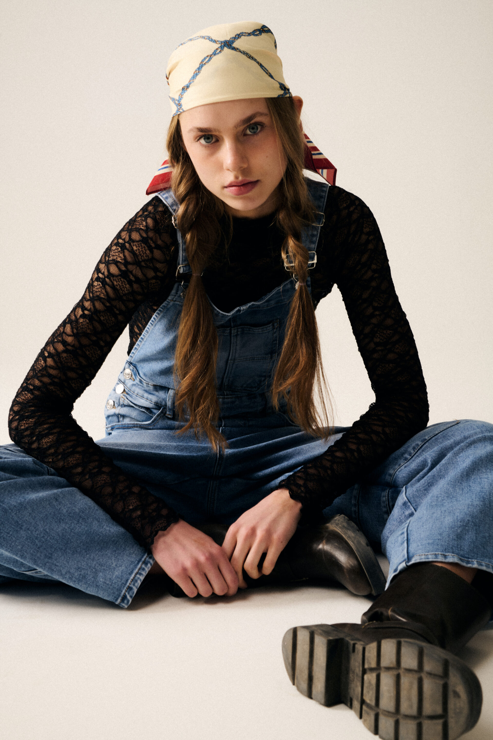 Chica sentada con un mono con la camiseta de encaje debajo con las manos hacia delante mientras fotógrafo le toma una fotografía