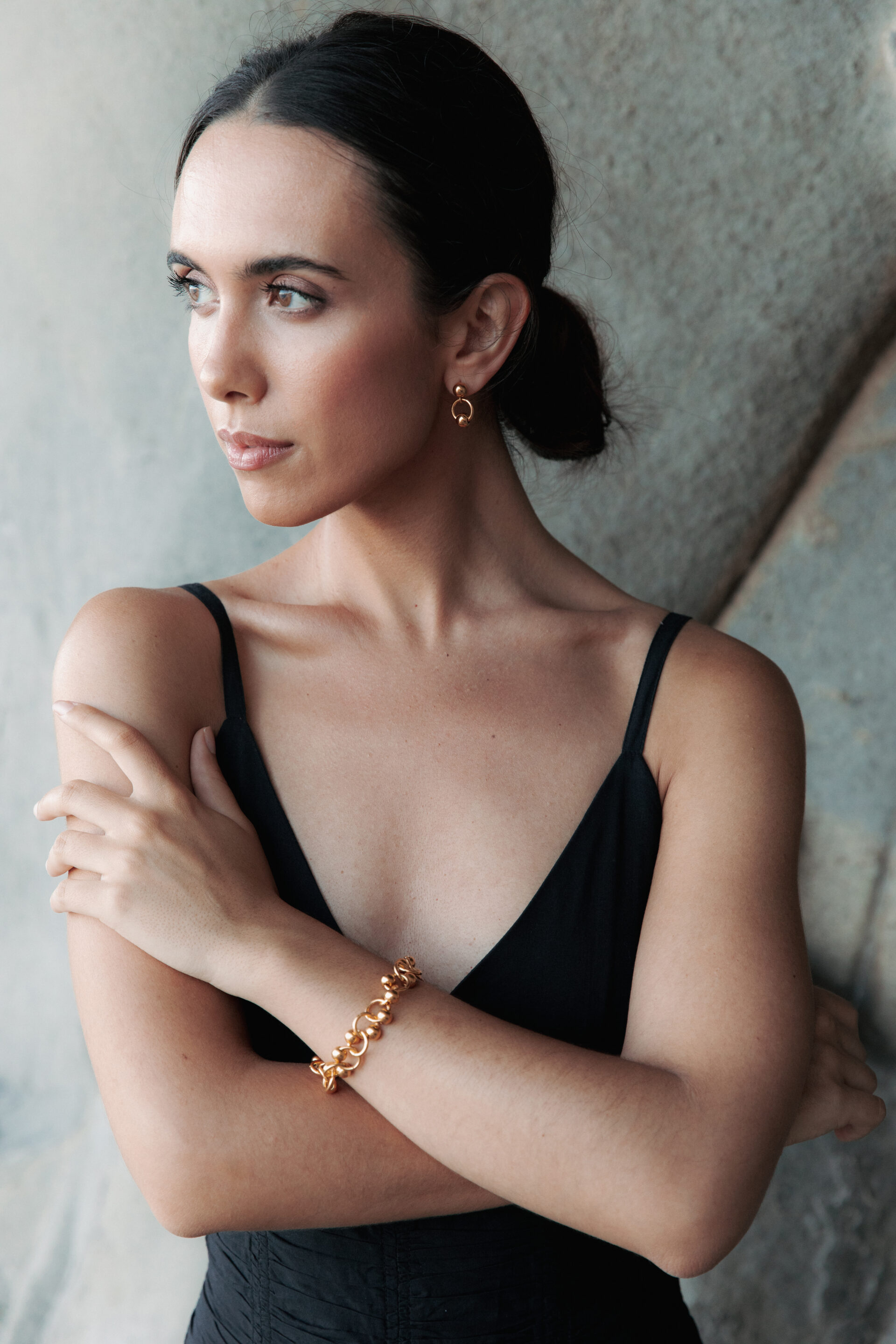 Chica con u vestido negro posando con los brazos entrelazados y delante de una pared de rocas mientras fotógrafo le toma una foto