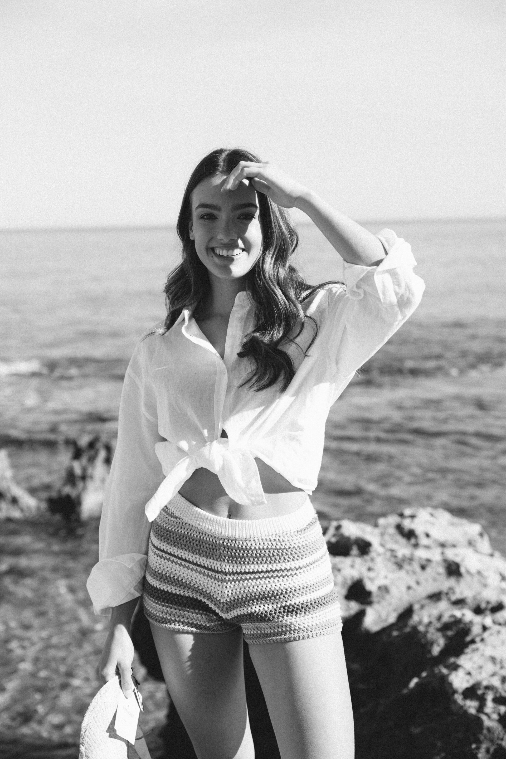 Chica posando en la playa con un sombrero vaquero mientras el fotógrafo le toma una fotografía en blanco y negro