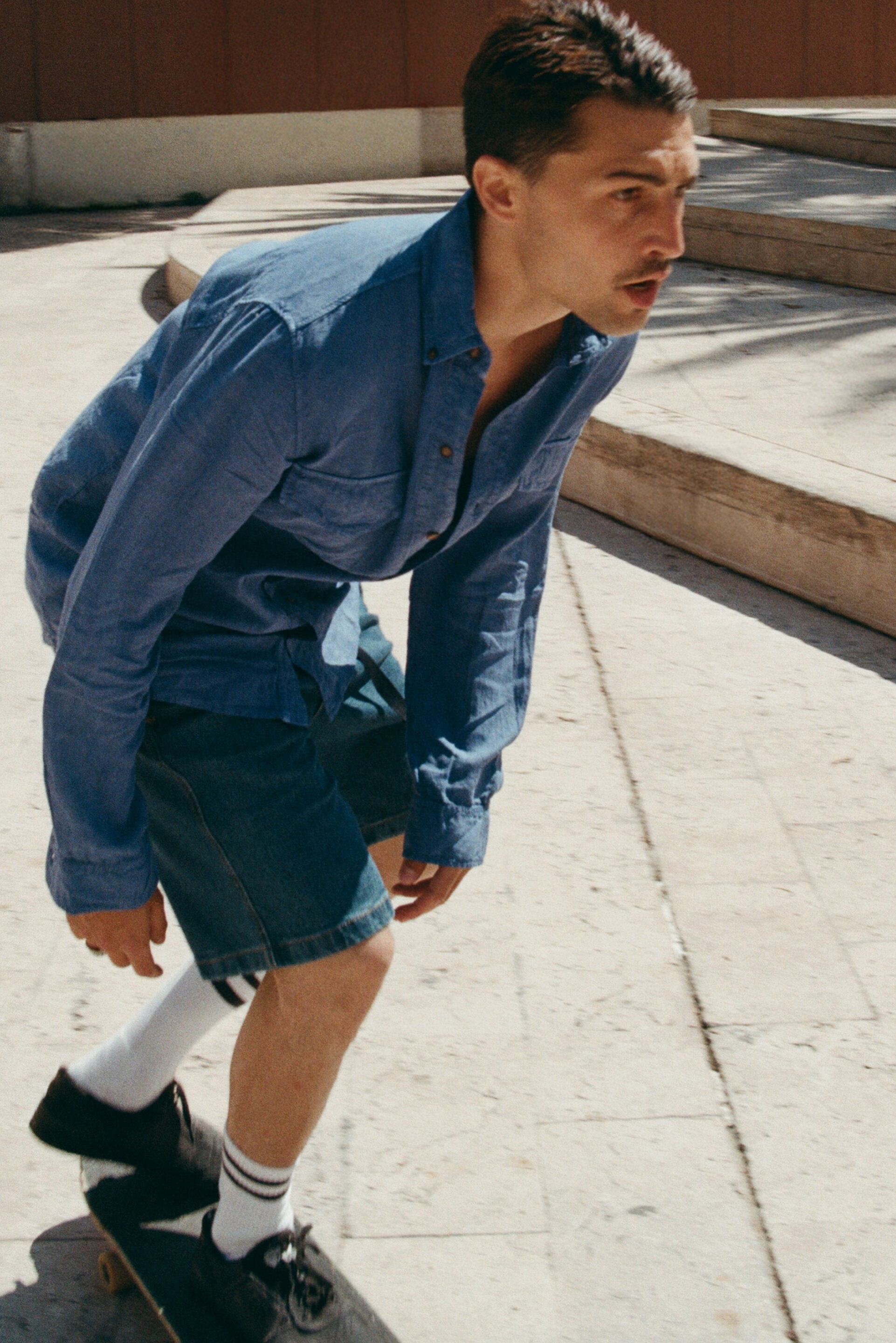 Chico en conjunto vaquero montando en skate mientras el fotógrafo le toma una foto